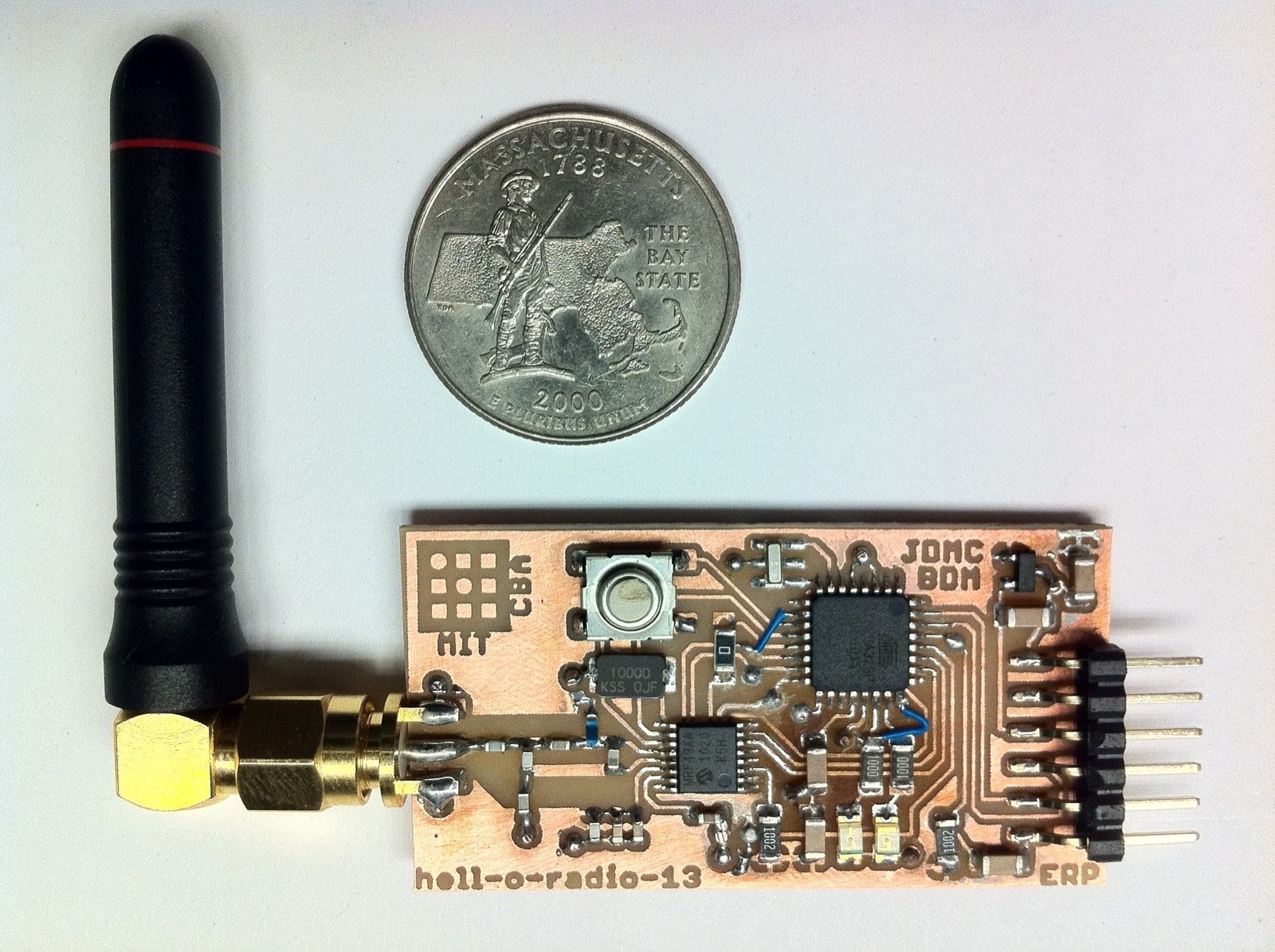 The milled Hello Radio board with its SMA antenna, shown beside a US quarter for scale